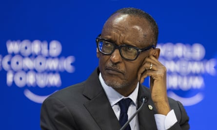 Paul Kagame, in a jacket and tie and with big-framed glasses and a gold ring, in front of a sign saying “World Economic Forum” holds a microphone to his ear and looks a bit concerned