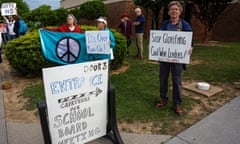 Demonstrators with a peace sign and placards say 'Stop glorifying civil war leaders' next to a school board meeting sign.