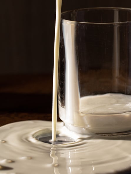 Milk pours over the side of a glass to form a circular pool.