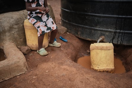 A girl sits on a jerrycan as another jerrycan is filled from a large tank