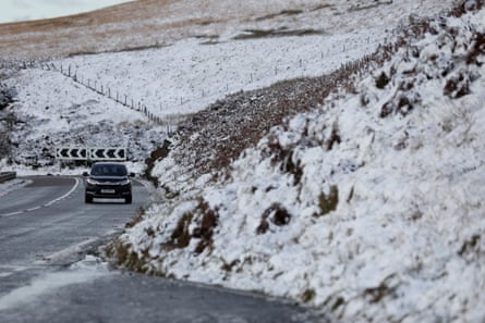 A car drives next to snowy moors on a hilly bend