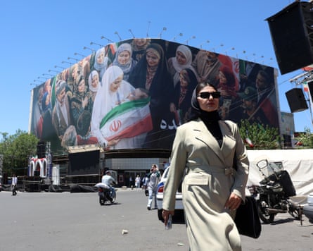 A woman walks next to a huge billboard in a street in Tehran