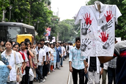 Crowds of Indians marching in a street with a white shirt in the foreground with red handprints on it held up a placard