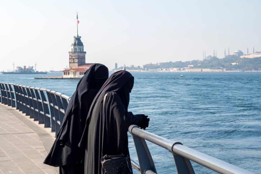 Two women dressed in traditional Muslim dresses with black hijabs look out over the Bosphorus Strait in Istanbul, Turkey