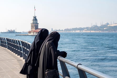 Two woman dressed in traditional muslim dresses with black hijab look out over the Bosphorus Strait in Istanbul, Turkey