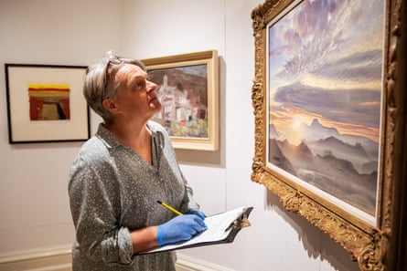 Woman writing notes on a clipboard as she inspects a painting on the wall