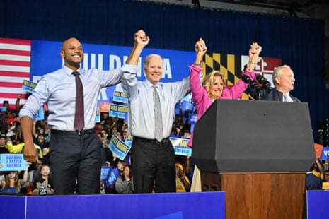 Wes Moore, Joe Biden, Jill Biden and Chris Van Hollen hold hands raised in victory at a rally where they are surrounded by supporters.