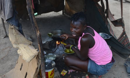 A teenage girl is cooks the family’s evening meal inside a makeshift tent of flattened cardboard boxes and cloth at a borderland encampment outside Anse-à-Pitres, Haiti.