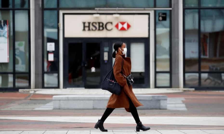 A woman wearing a face mask walks past a HSBC bank in La Defense near Paris