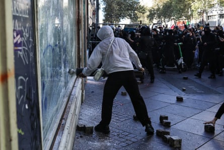 A protester in a white hoodie smashes a window during a Marseille demonstration