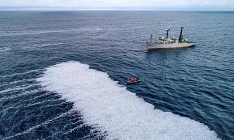 A ship and a small dinghy next to a white mass on the sea perhaps 100 metres long of dead fish