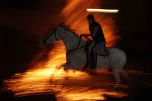 Men ride horses through the bonfire made with pine tree branches