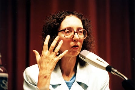 Oates speaking into a microphone with one hand raised and a red curtain behind her
