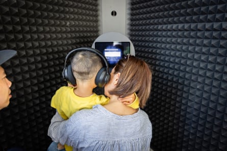 A woman holding a young child with headphones as they record a message in a recording booth