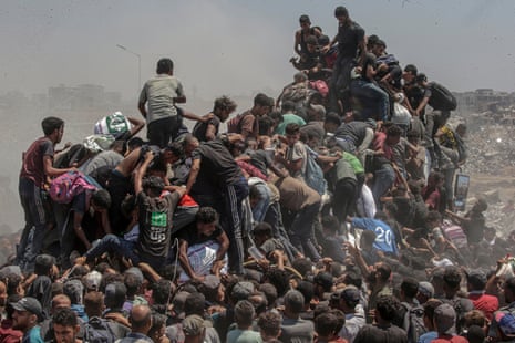 Displaced Palestinians scramble on top of a truck, reaching for aid supplies in Gaza