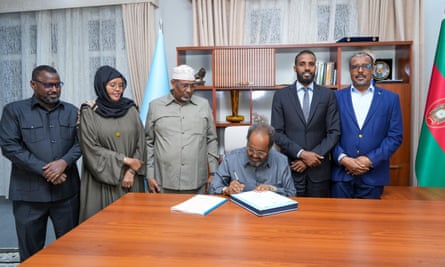 Ministers stand either side of the seated president as he signs a document.