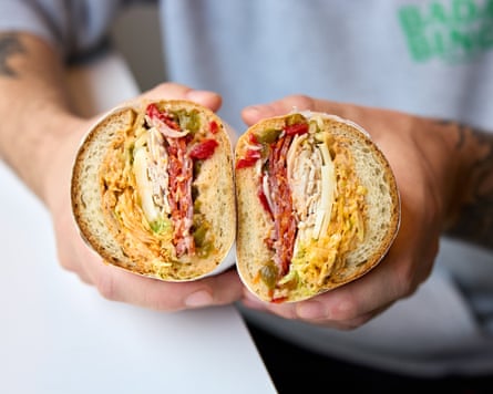 A man holding a sandwich cut in half, showing the filling
