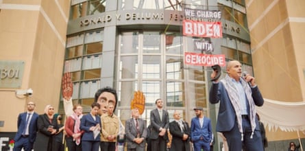 man speaks into mic in front of sign that says ‘we charge biden with genocide’