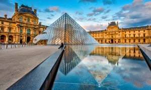 There is a blue sky with the reflection of the Museum Louvre with the Pyramid