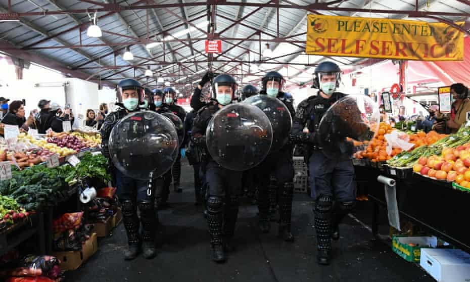 Police with transparent shields walk down an aisle of fruit and vegetables  atQueen Victoria Market during an anti-lockdown protest in Melbourne