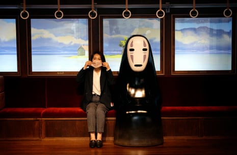A Ghibli Park visitor sits next to the No-face (Kao-nashi) character from the movie Spirited Away.