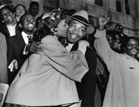 a black and white photo of a woman kissing a man’s cheek as people cheer around them