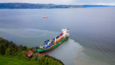 Aerial view of the container ship's bow nosed into the shoreline by a house.
