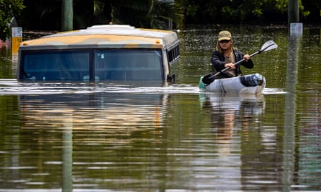 A man paddles his kayak next to a submerged bus on a flooded street in the town of Milton in suburban Brisbane