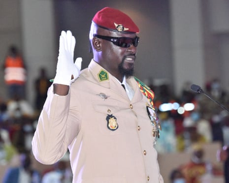 Doumbouya raises his hand at his swearing-in ceremony as interim president, 1 October 2021, in Conakry. He wears a pale military jacket with medals, white gloves, a red beret and black sunglasses