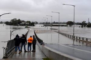 Members of the public look on as the Windsor Bridge is submerged under flood water from the Hawkesbury River