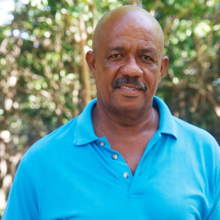 A middle-aged moustachioed black man looks at the camera