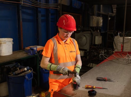 A worker wearing a hard hat and hi-vis jacket uses a tool to remove a battery from a disposable vape