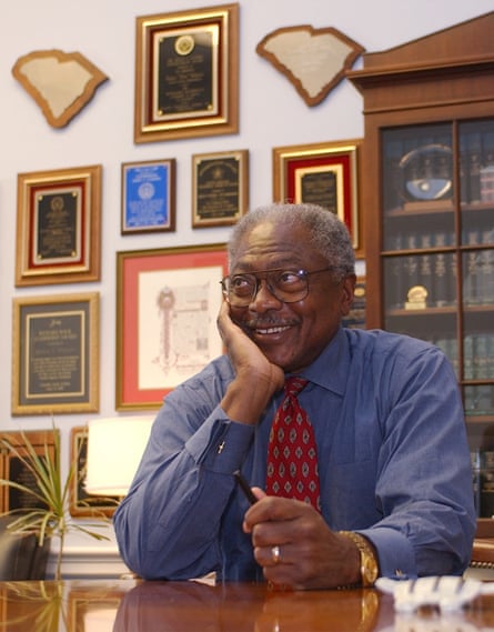 An older man smiles as he sits at a desk.