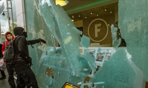A protester smashes the front window of Foxton, an estate agency, which is perceived as part of the problem of gentrification of Brixton.