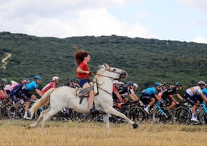 A woman rides a horse next to the Peloton during the 12th stage of the Tour de France 2021 over 159.4 km from Saint Paul Trois Chateaux to Nimes