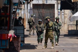 A soldier points his automatic weapon as he and four colleagues walk down a street