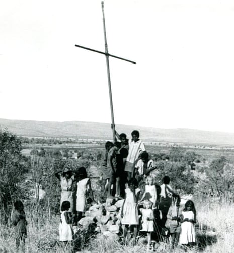 Children stand below a wooden cross on a pile of stones