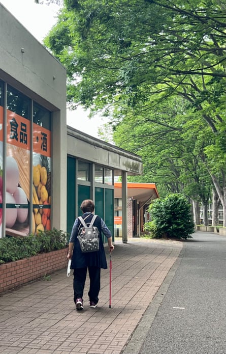 A woman walks along a tree-lined walkway next to a shop with a stick