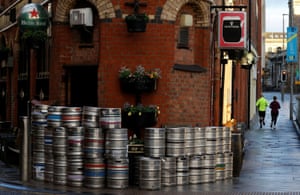 Belfast, Northern Ireland: people run past stacked empty beer barrels outside a closed pub