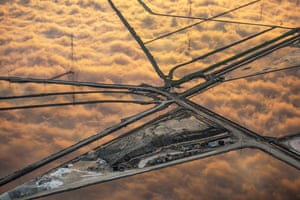 Clouds are reflected in the still water of large salt ponds around a triangle of land with raised roads and paths bisecting the water