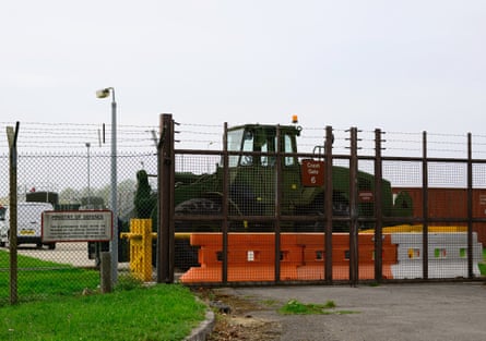 A heavy vehicle parked behind a gate. The fencing has barbed wire on top of it
