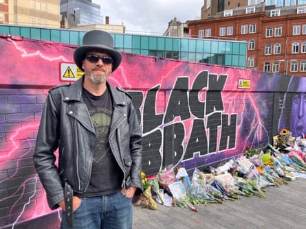Fan Will Taylor next to a wall where flowers have been laid for Ozzy Osbourne’s funeral procession