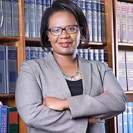 A middle-aged African woman in a suit standing before a law library bookcase