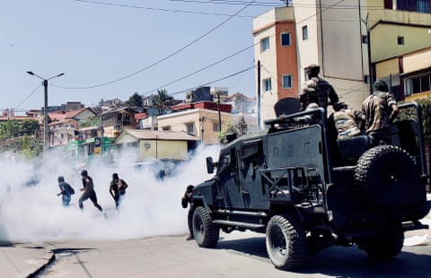 An armoured truck amid smoke, and protesters running away