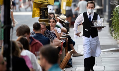 A waiter wearing a face mask serves customers at tables outside a restaurant in Soho, London