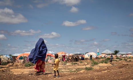 Woman and young child stand looking at tents in the distance
