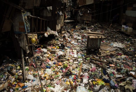 A boy is barely seen amid an expanse of plastic and other waste between shacks