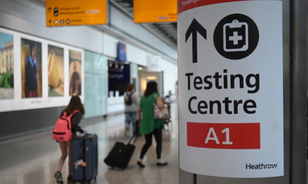 Passengers push their luggage past a sign displaying the way to a Covid-19 test centre, in Terminal 5 at Heathrow airport in London.