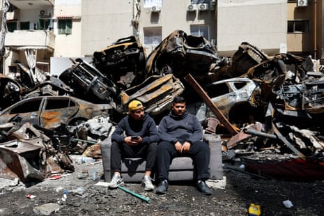 Двое мужчин сидят на сером диване перед обломками и обломками.