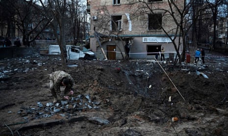 A Ukrainian solider collects missile fragments in a crater left by a Russian attack beside a residential building in Kyiv